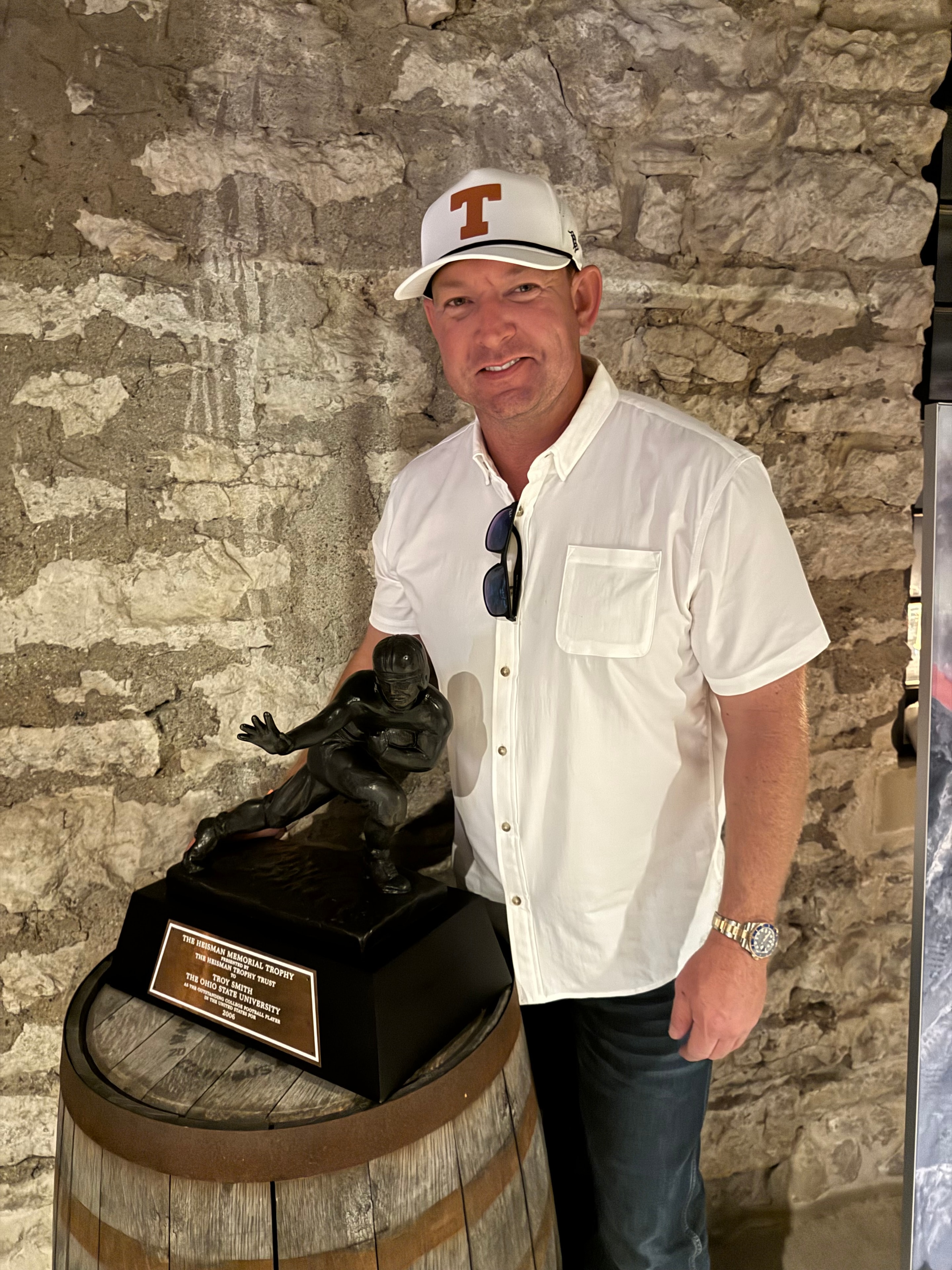 Man in Texas Longhorns cap posing with Heisman Trophy